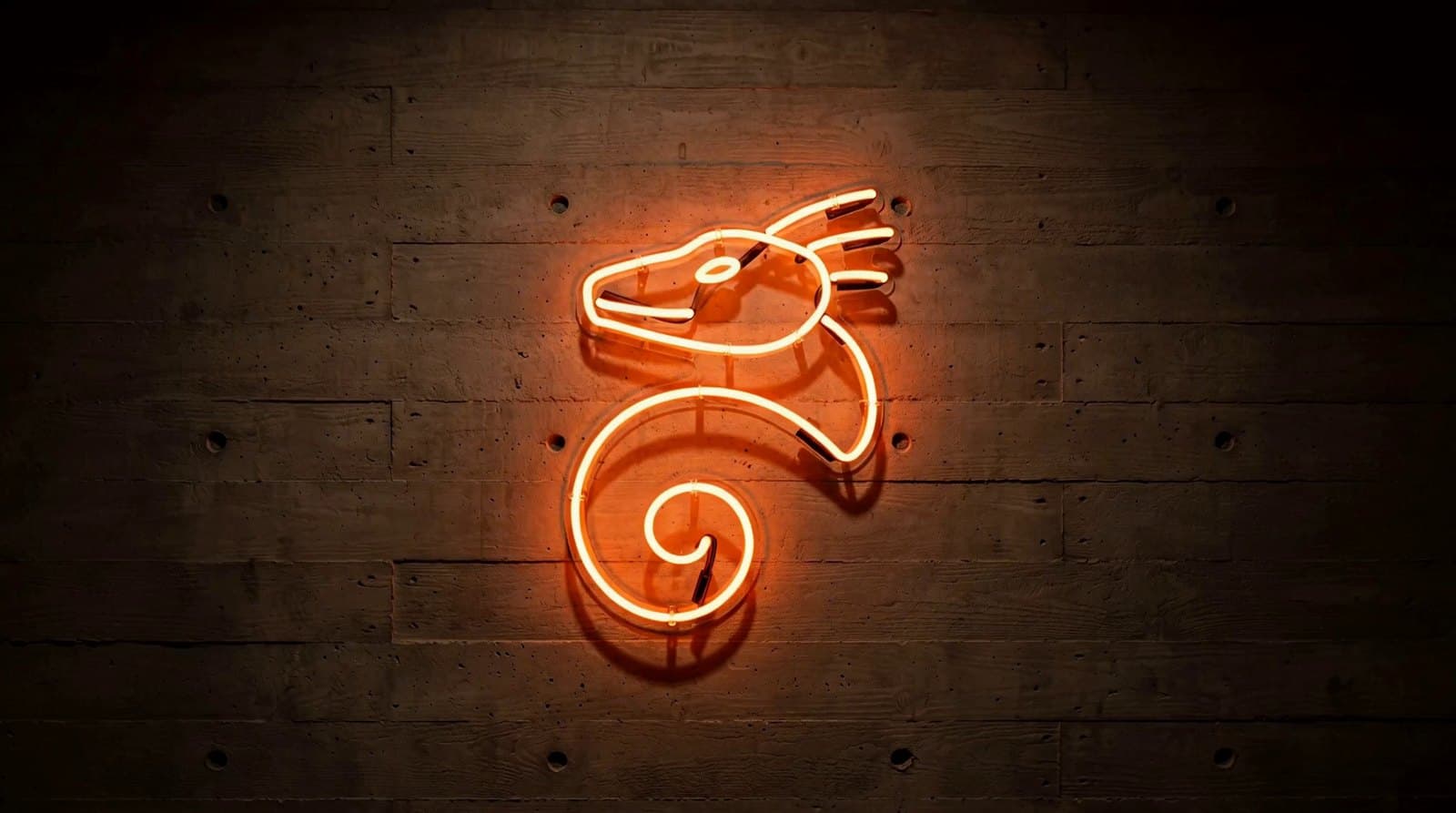 The Guardian mark as a hand-bent ember neon sign on a board-marked concrete wall at night